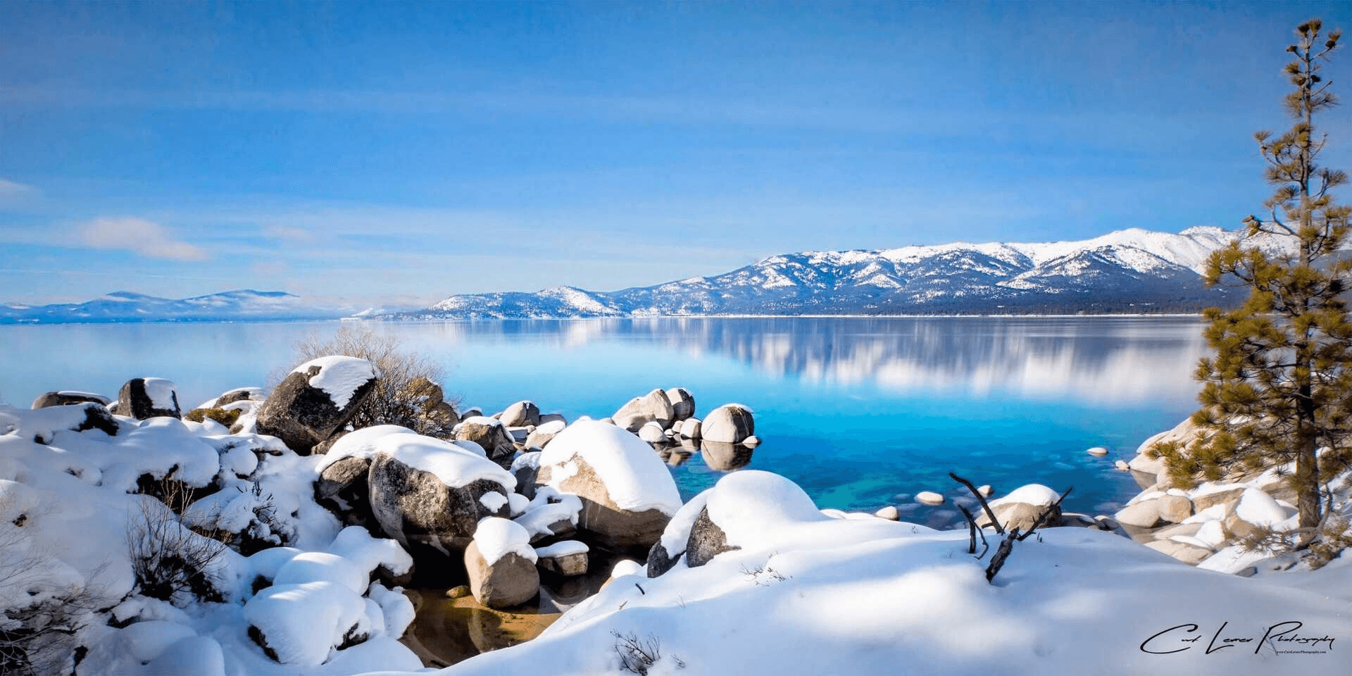 Snow-covered rocks along a bright blue Lake Tahoe shoreline